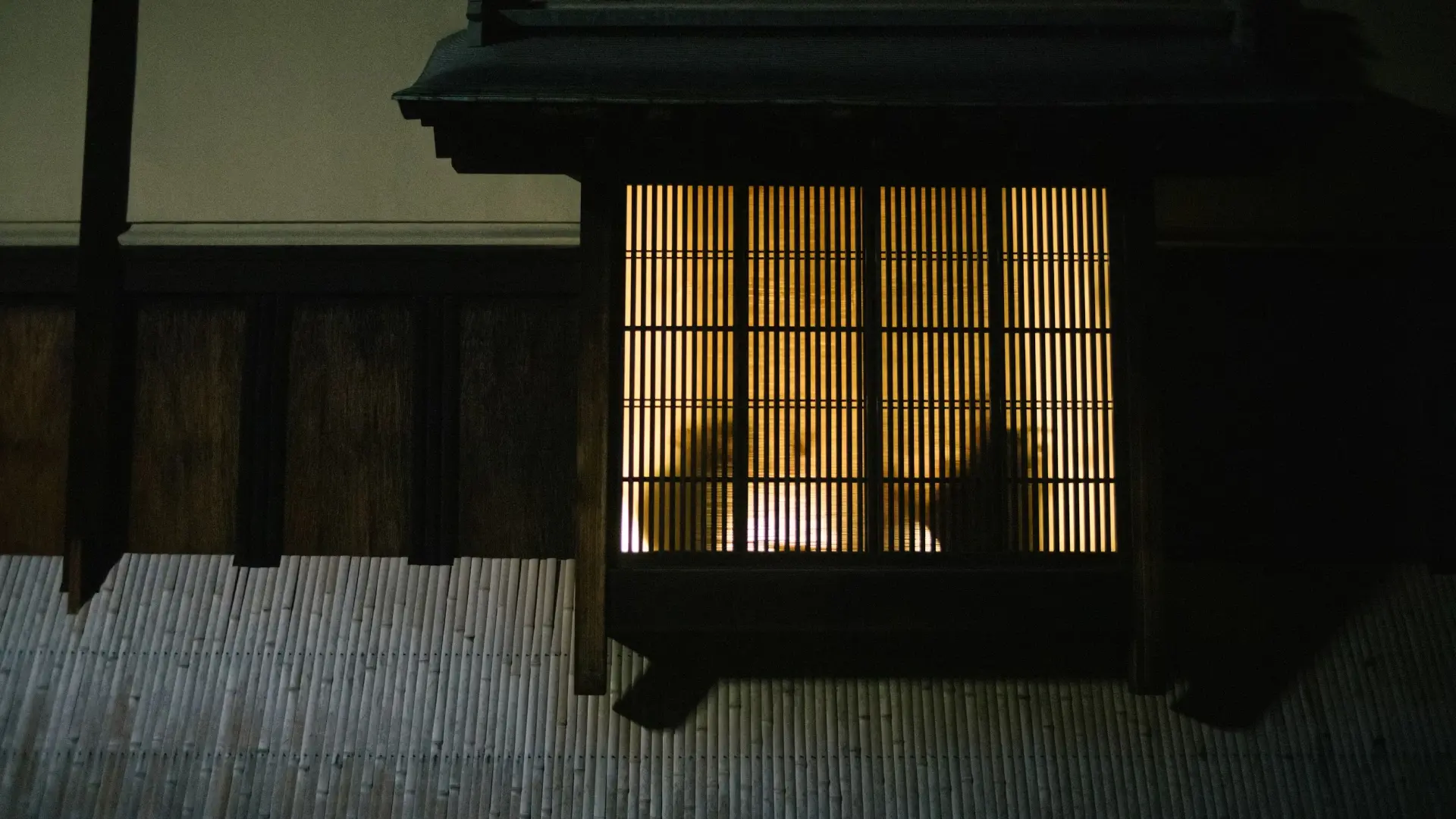 Warm amber light glowing through the wooden lattice window of a traditional Japanese building at night