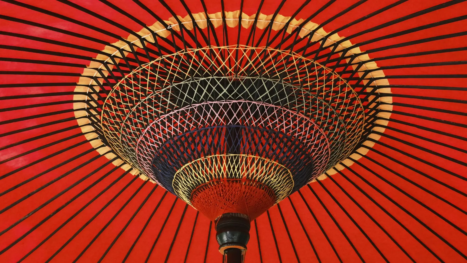The intricate spoke pattern and vivid red washi paper of a traditional Japanese wagasa umbrella seen from below