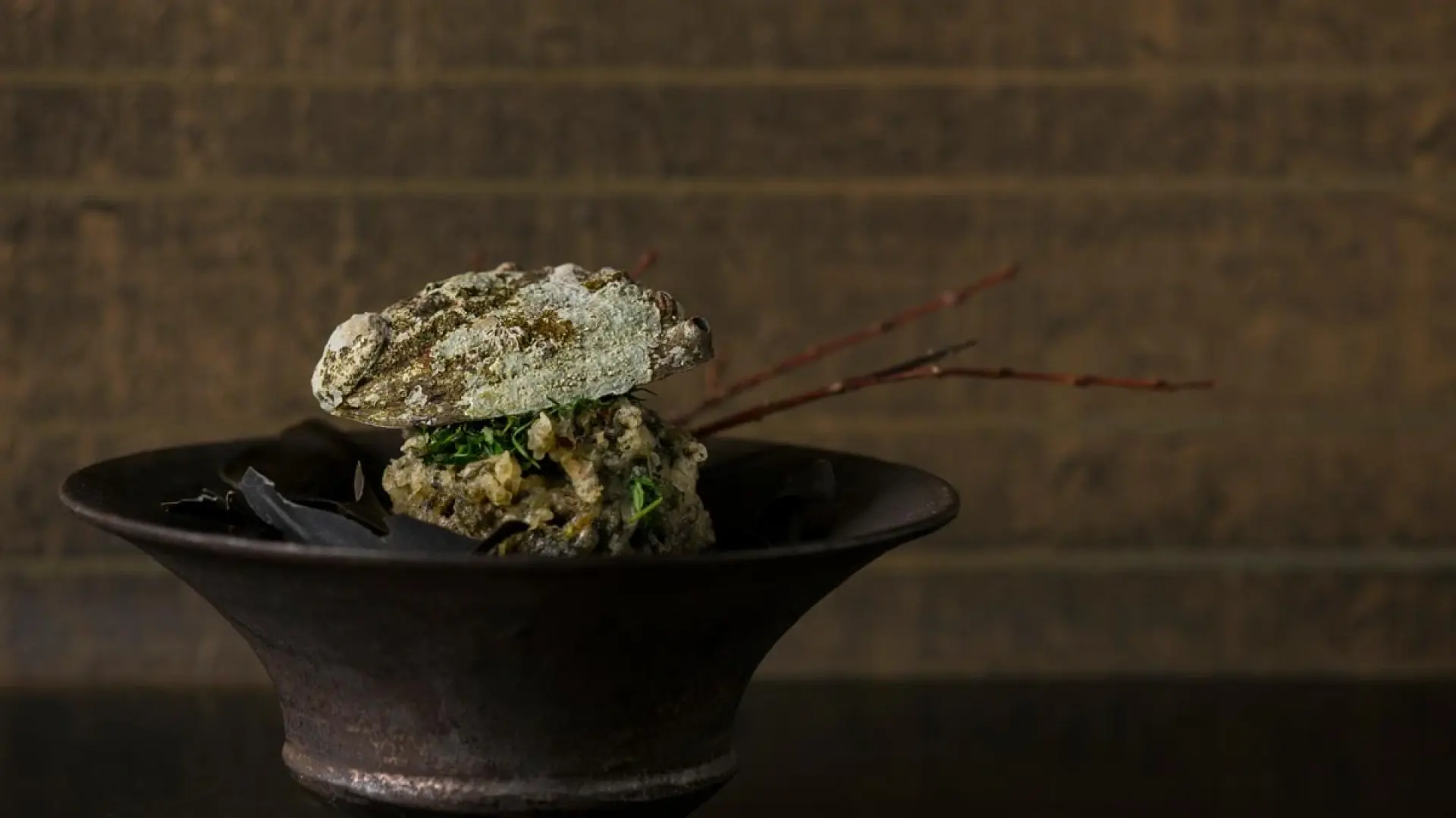 An artfully plated tempura dish served on a dark handcrafted ceramic bowl with decorative branches