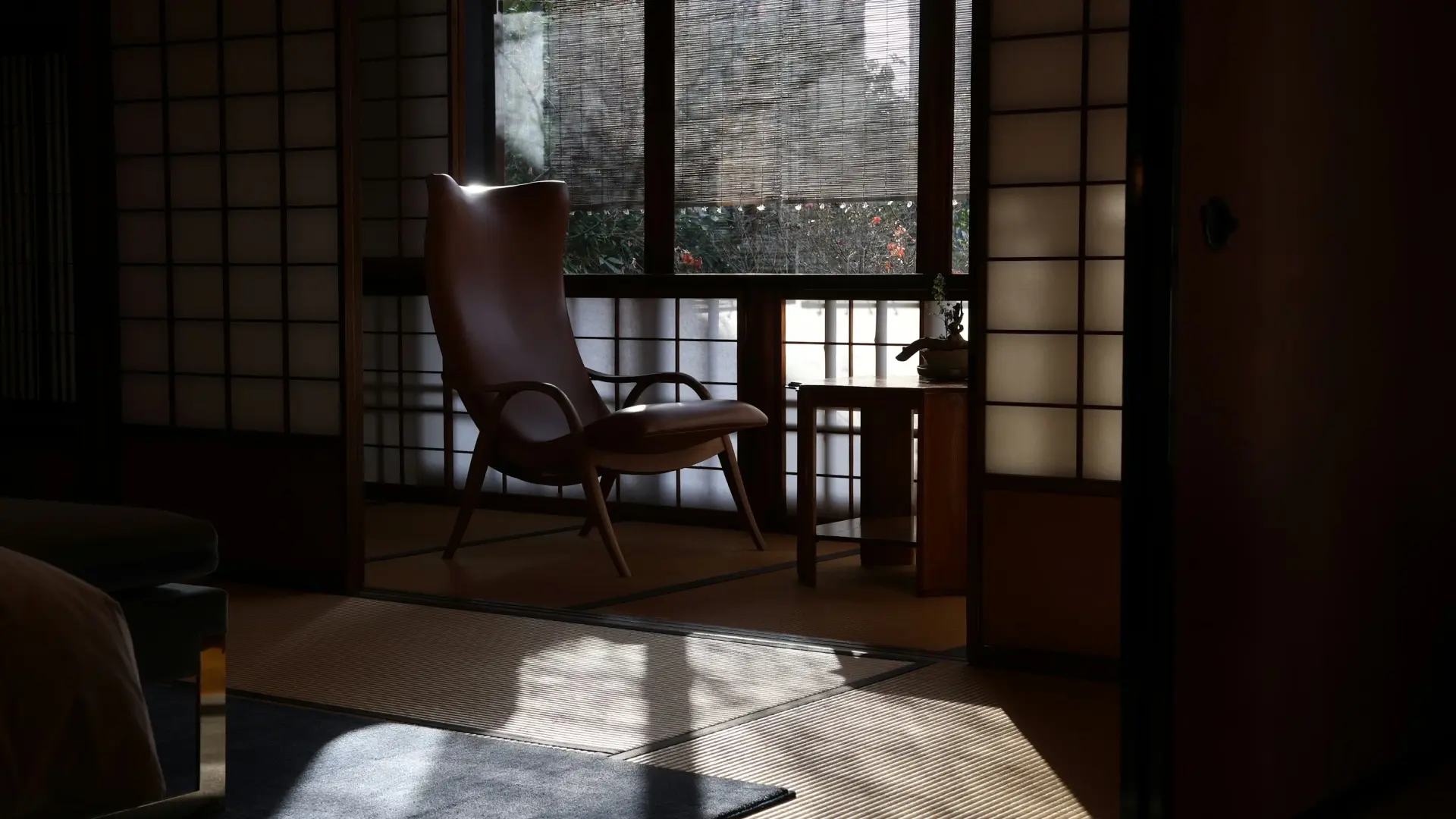 A designer chair silhouetted in a tatami room with soft light filtering through shoji screens and a bamboo blind