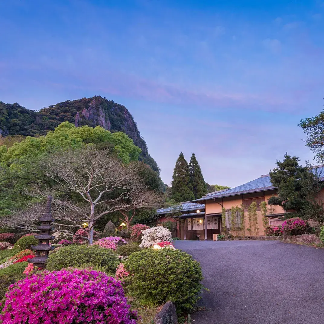 Onyado Chikurintei entrance framed by azaleas and Mount Mifune at dusk in Takeo