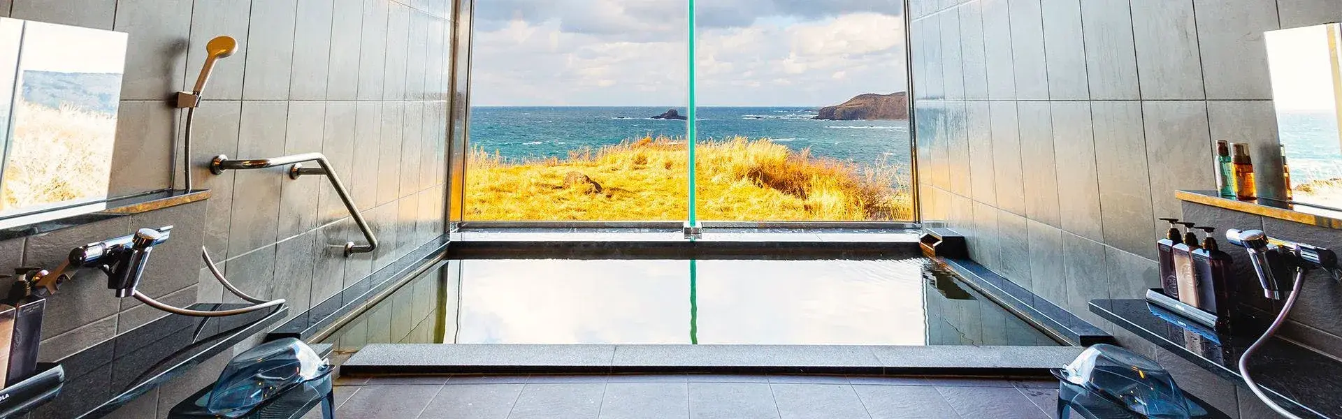 Glass-walled indoor bath overlooking the Sea of Japan and rocky Oga coastline
