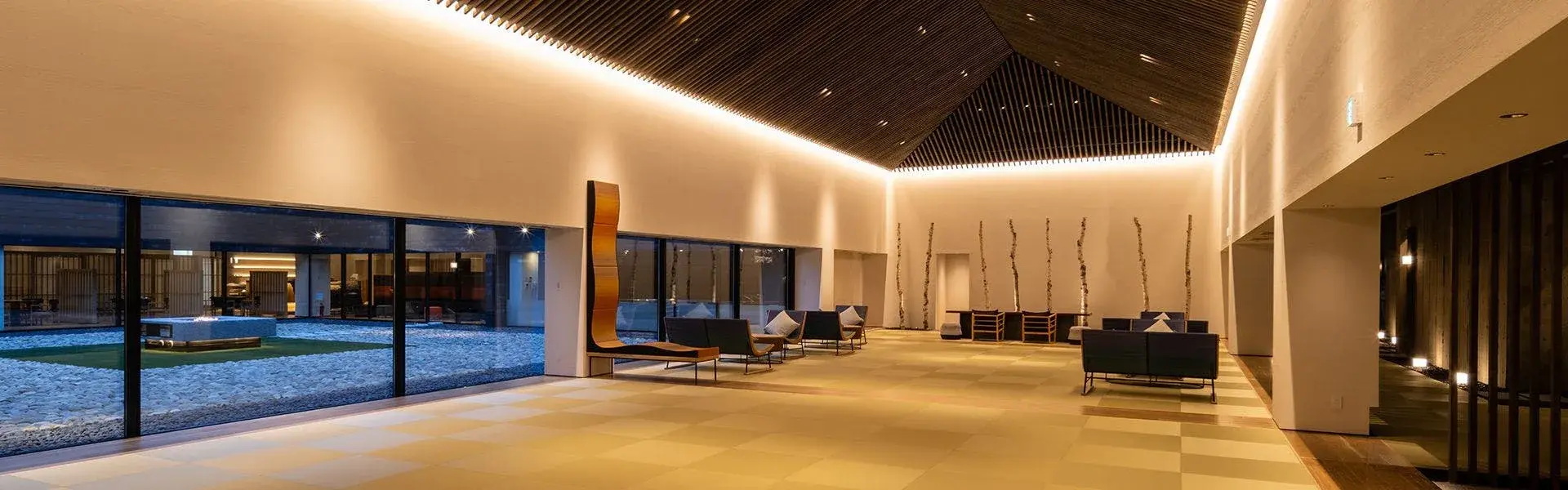 Seijyakubow's grand lobby at night, larch timber gabled ceiling and gravel courtyard beyond