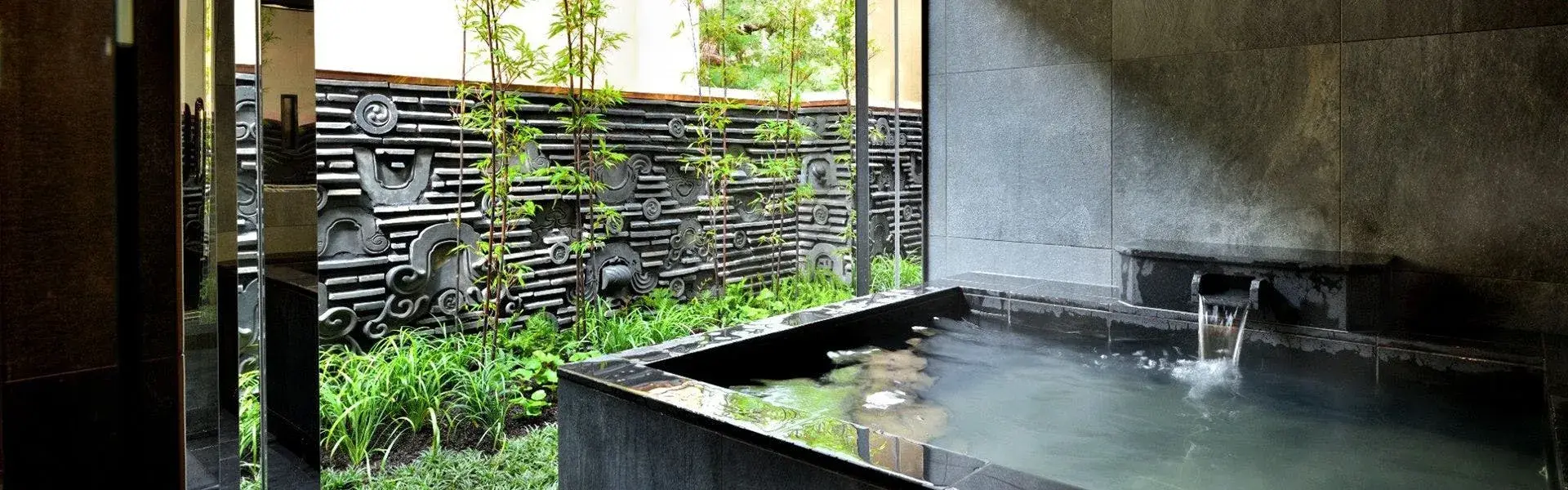 Stone private bath with carved decorative wall panel and bamboo garden at Tsuruko