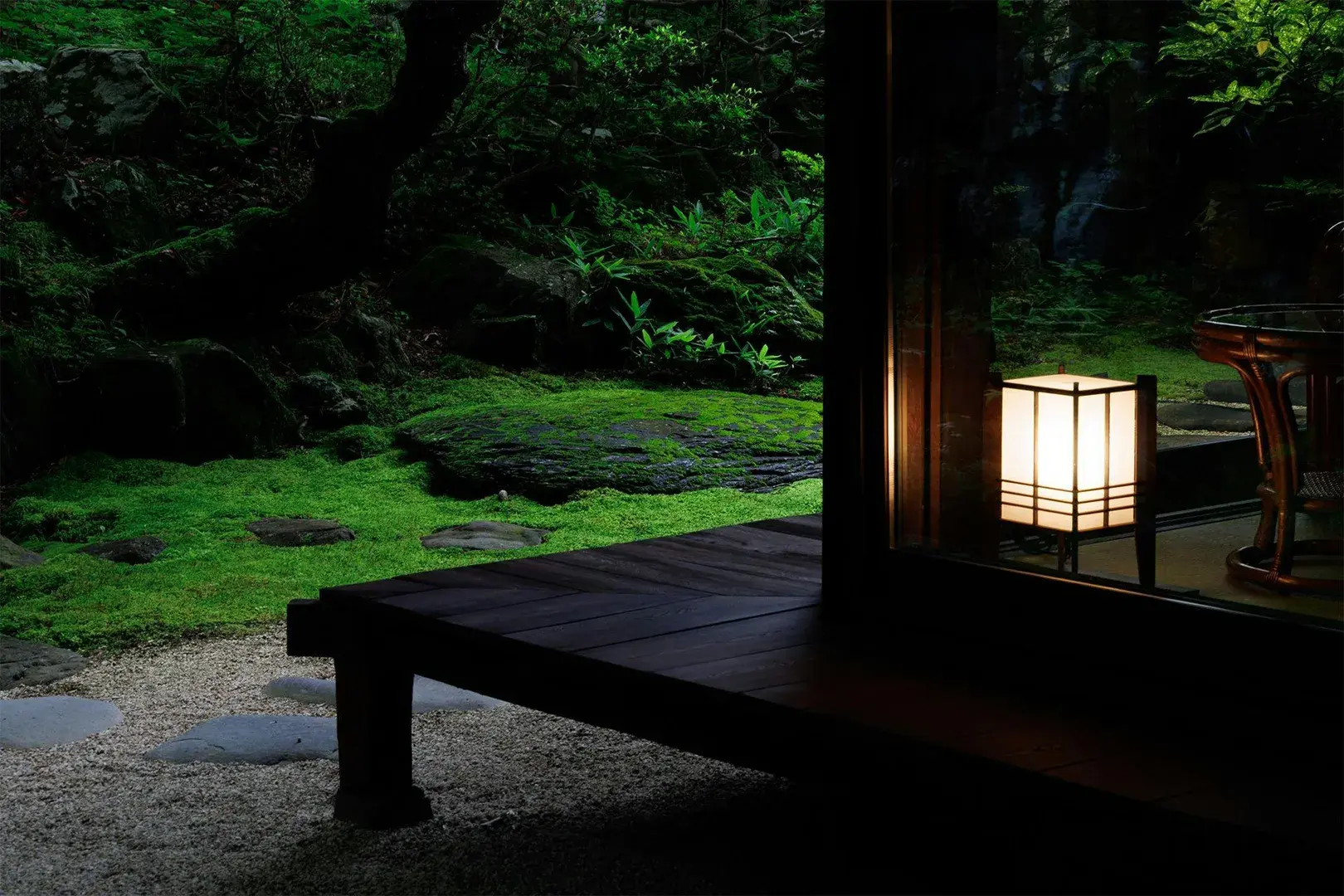 Stone and moss garden at dusk lit by a shoji lantern