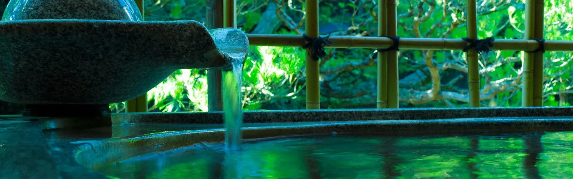 Stone basin pouring onsen water into an indoor bath at Hanaougi Bettei Iiyama, Takayama