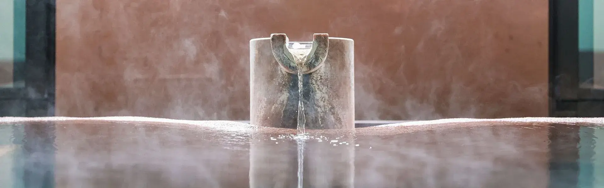 Hot spring water pouring from a stone spout into an Izu onsen bath