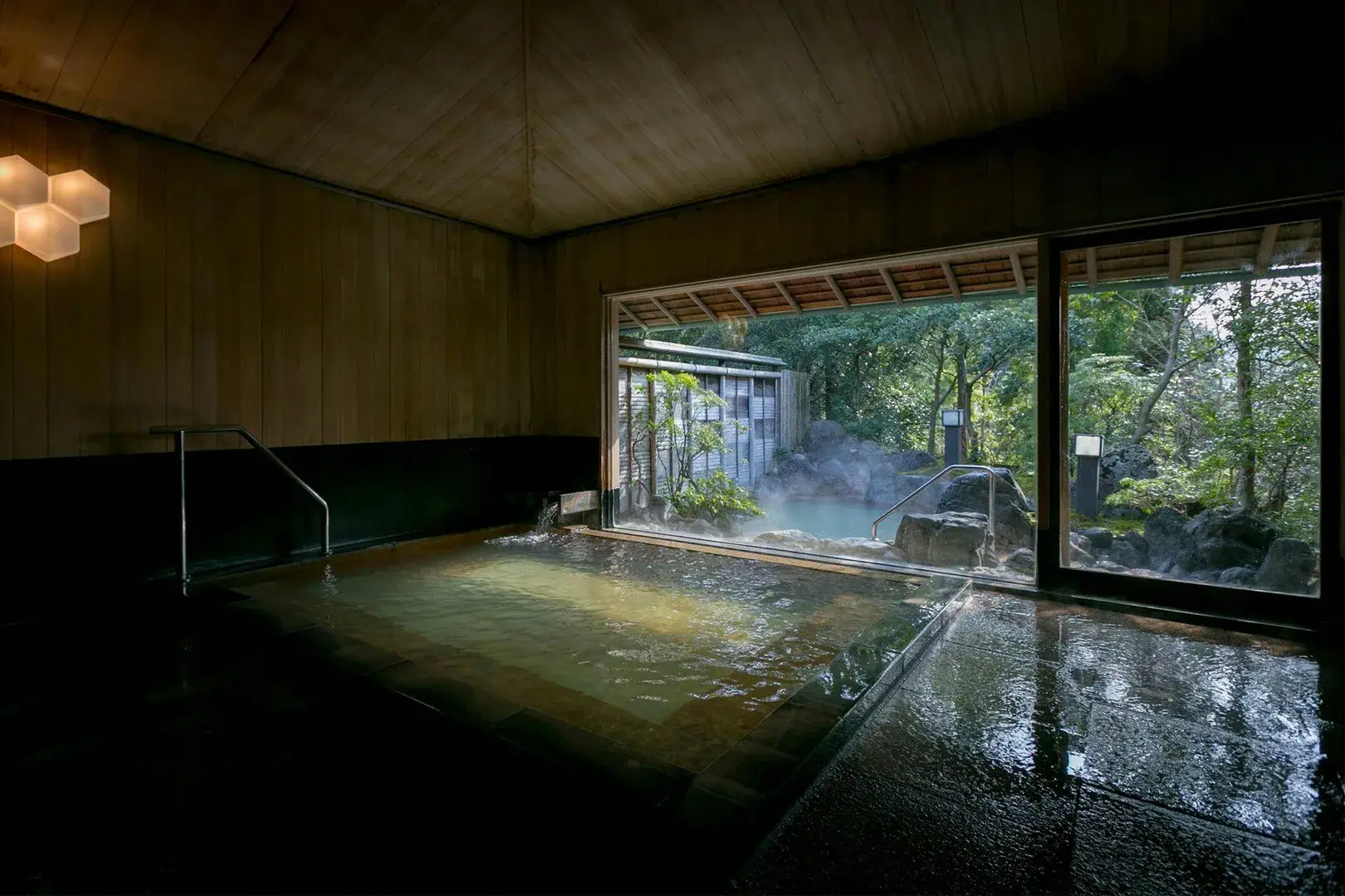 Indoor onsen bath opening to a steaming rotenburo and rock garden