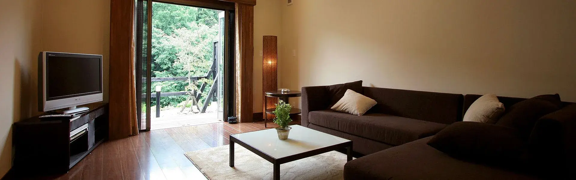 Cottage sitting room with dark sofa and forest-facing terrace in Nikko