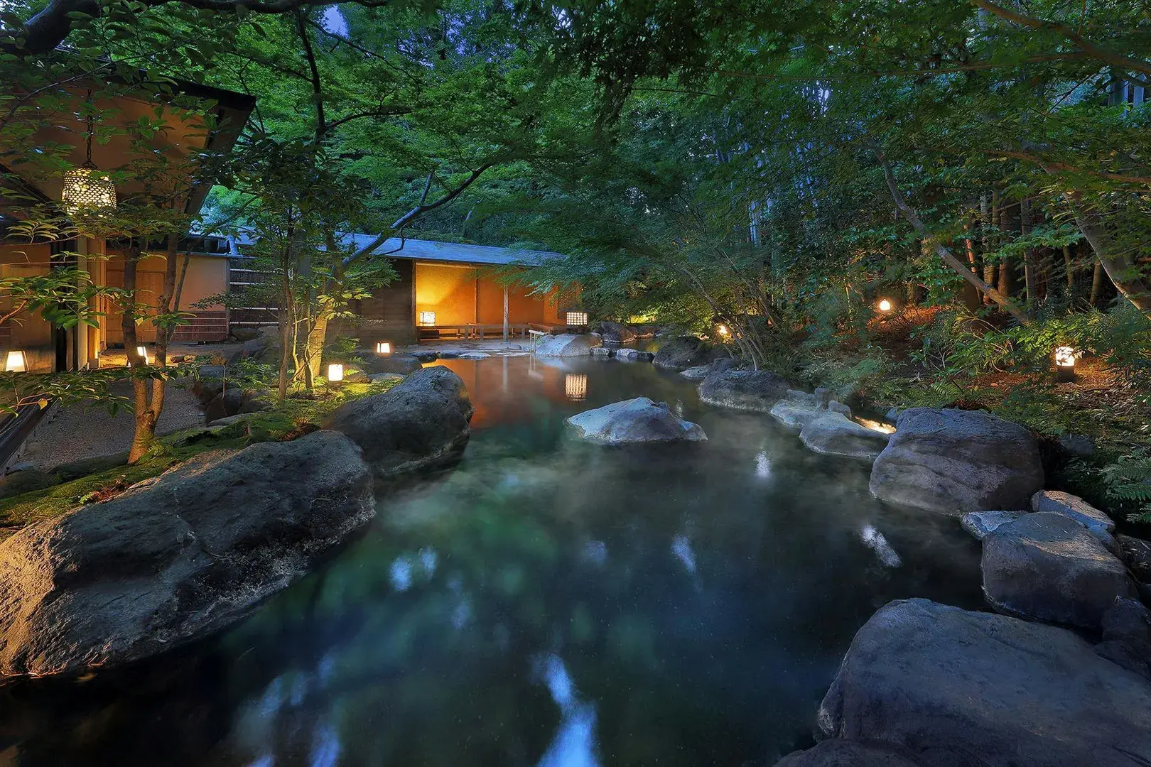 Rock-edged rotenburo outdoor onsen glowing at night in Shuzenji