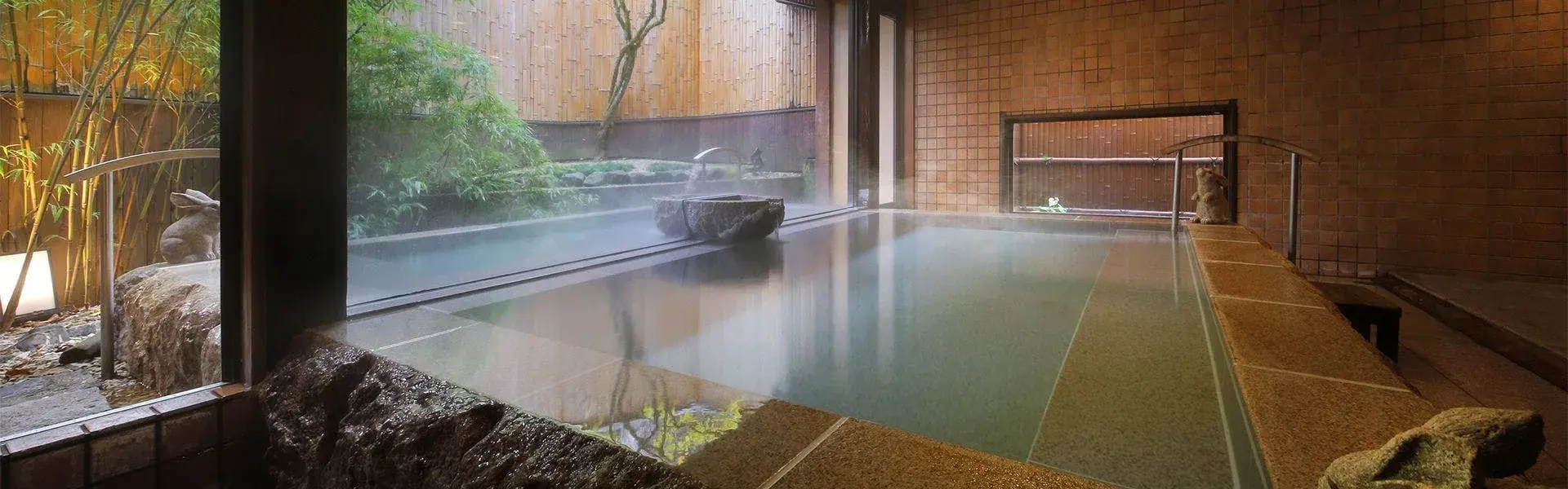 Kuhe Ryokan's indoor onsen bath steaming beside a bamboo garden