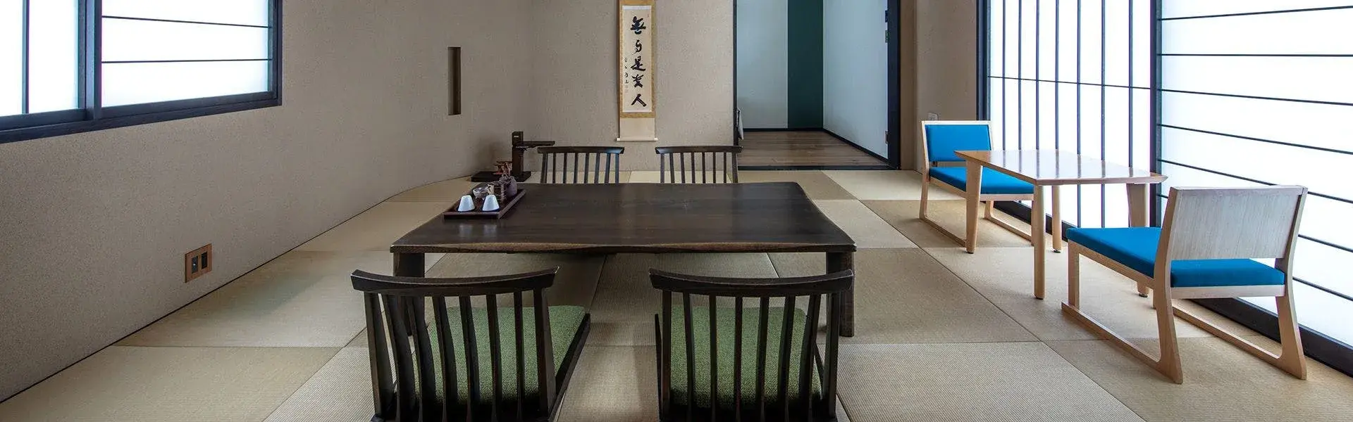 Tatami room with low dining table, calligraphy scroll, and blue accent chairs at Zabou