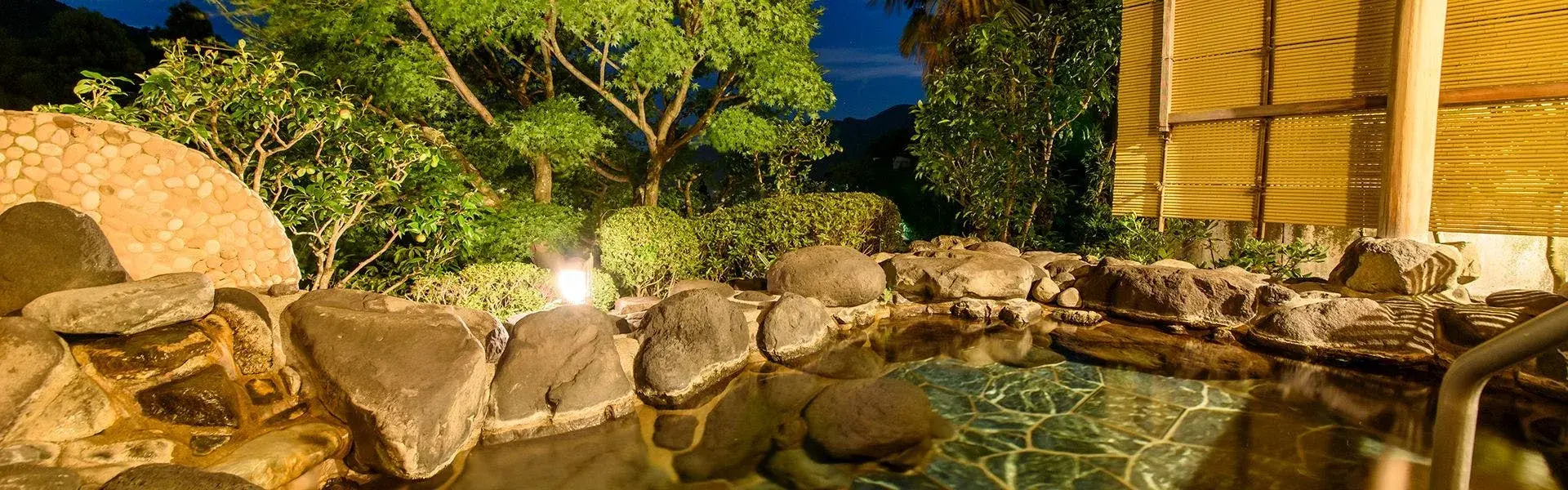 Oyado Zuigetsu's rock-edged rotenburo glowing beneath a garden of illuminated pines at night