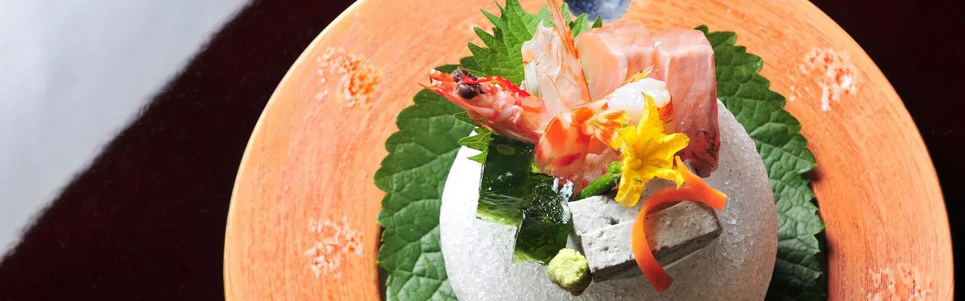 Sashimi course with red prawn, tuna, and edible flower on a stone pedestal