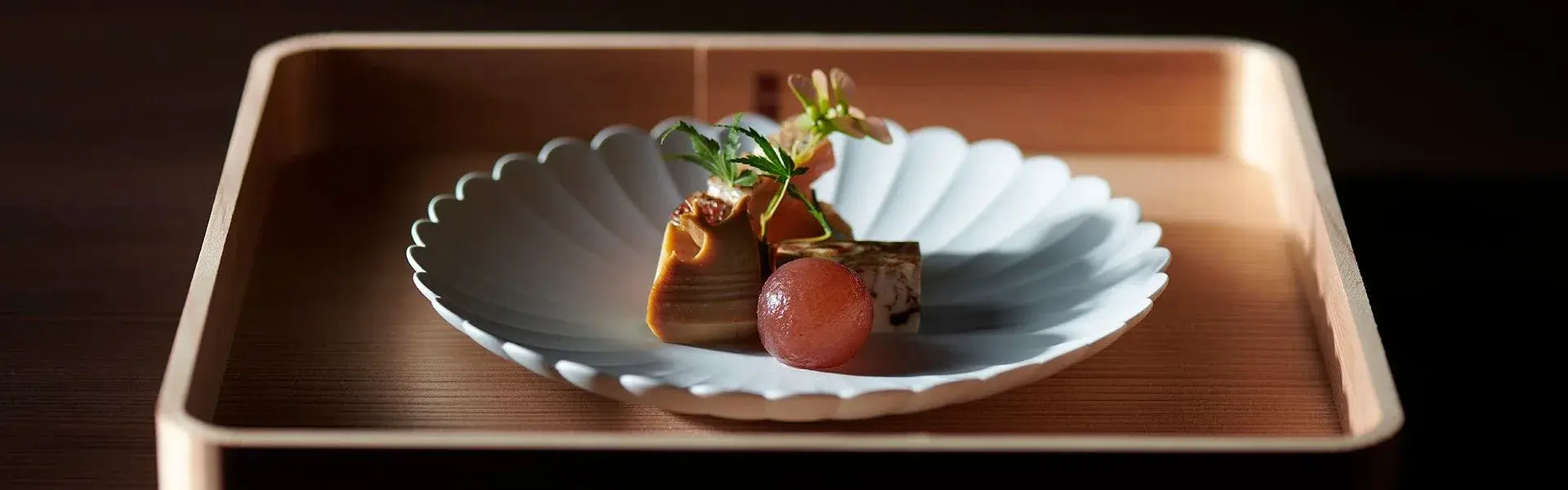 Kaiseki course on white scalloped ceramic with braised morsel and red tomato