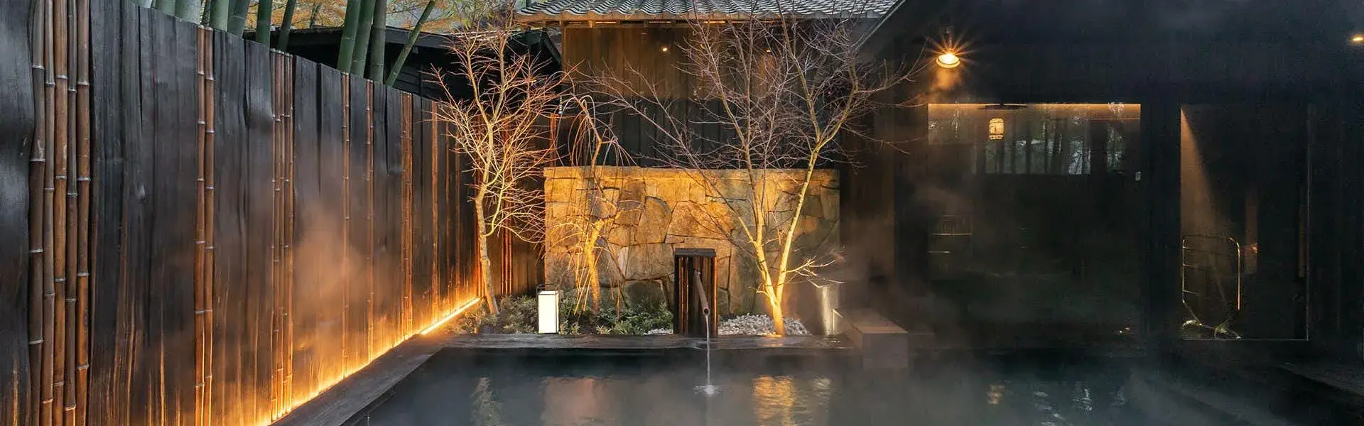 Steaming rotenburo at night beside Takefue's illuminated bamboo fence in Aso