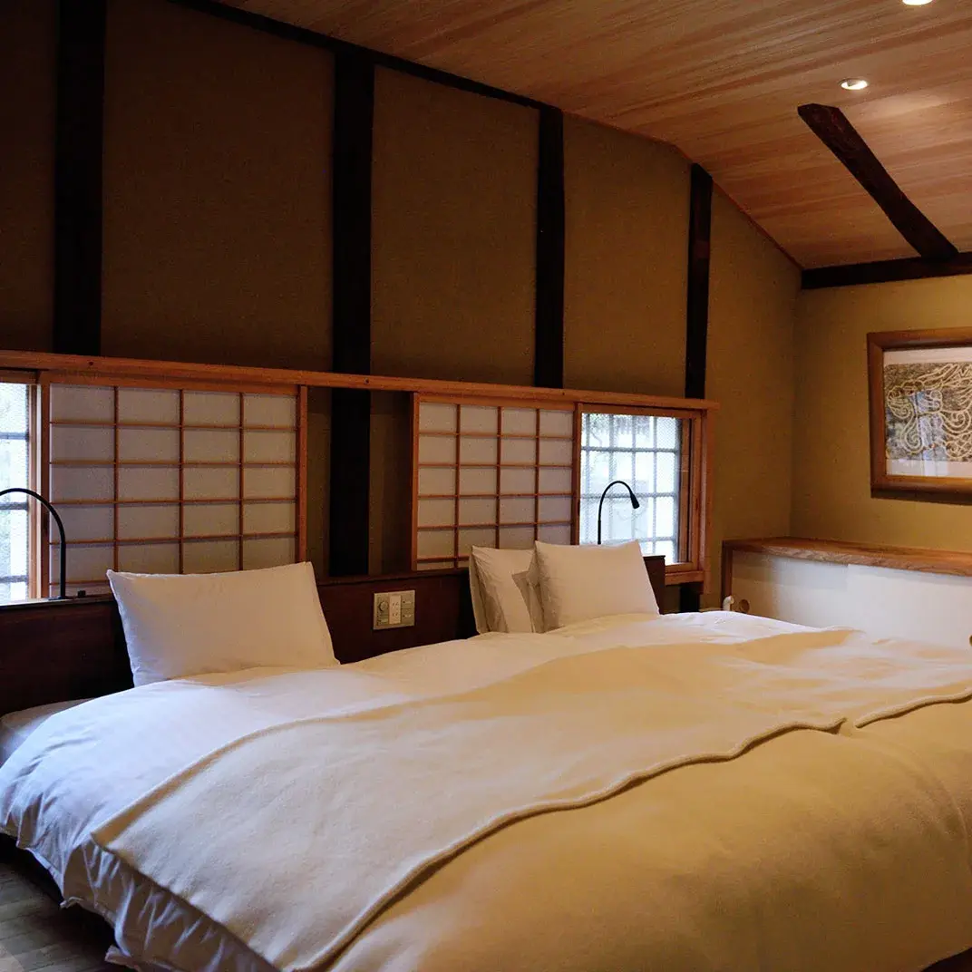 Twin room with shoji screens under cedar beams at Ryokan Kurashiki
