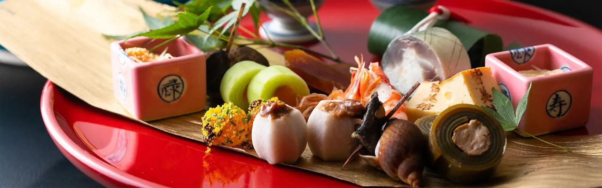 Kaiseki appetizer course on red lacquer tray with seasonal shellfish and bamboo vessels