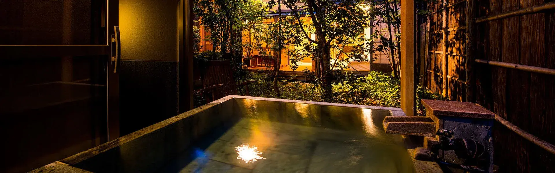 Stone rotenburo glowing under illuminated garden trees at Akayu Onsen after dark