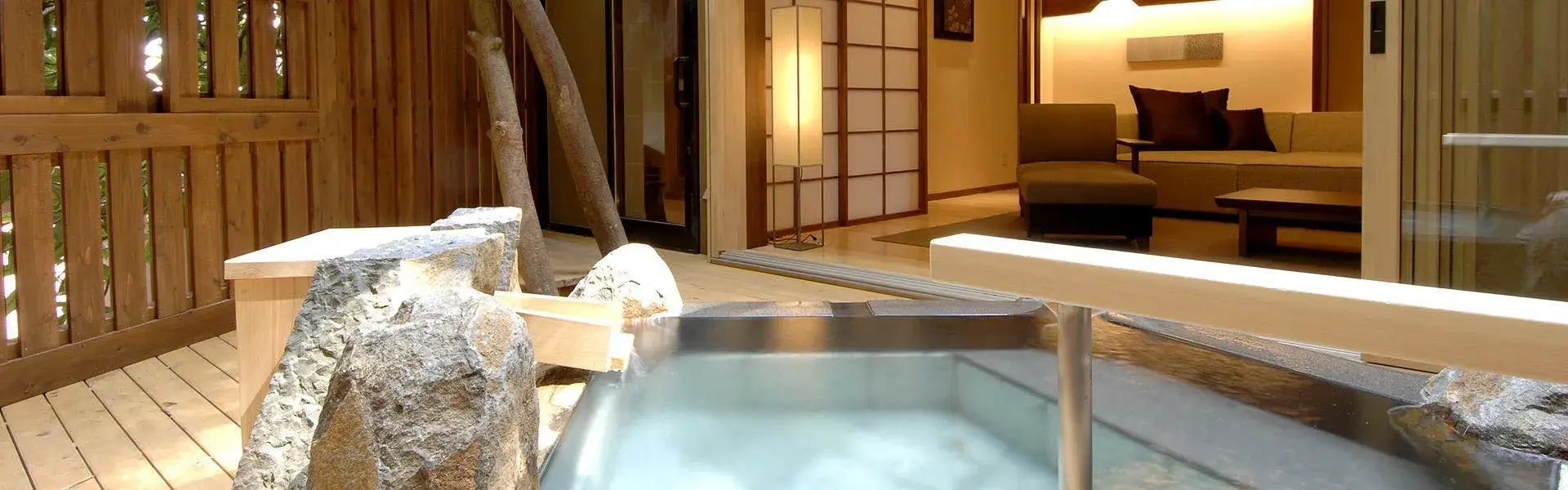 Private in-room rotenburo with stone basin on cedar deck, shoji-screened lounge beyond