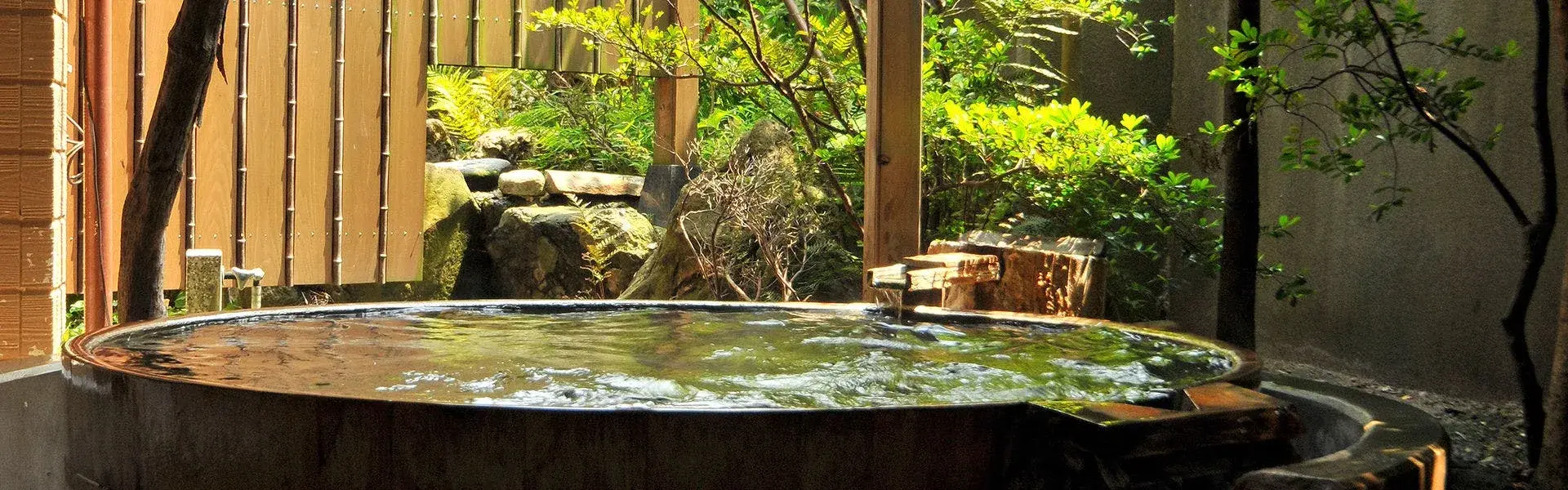 Circular hinoki barrel rotenburo fed by Tsukioka Onsen spring water, enclosed by timber screen and garden rocks