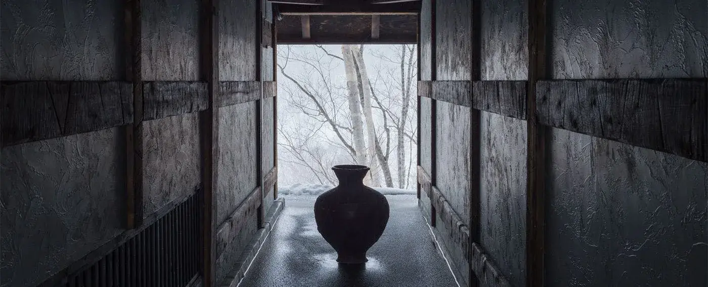 SHIGUCHI's kominka entrance corridor with ceramic vessel and snowy Hokkaido forest beyond