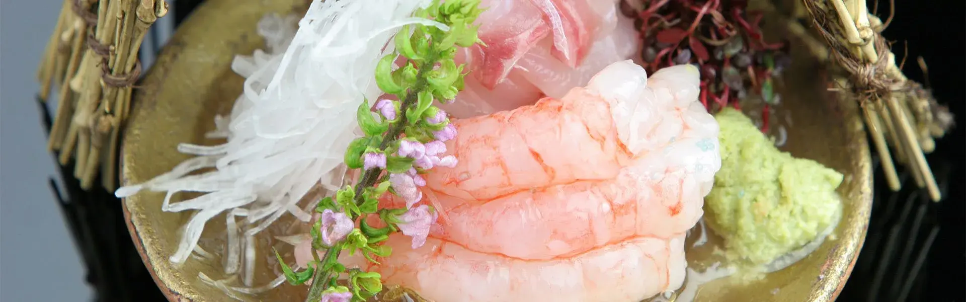 Sweet shrimp sashimi with wasabi and flowers on a gold-rimmed kaiseki dish
