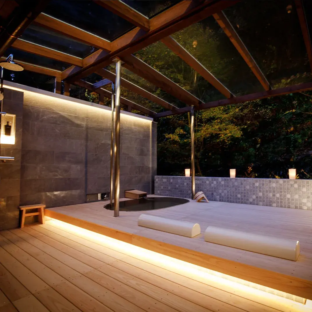 Private rotenburo at night on cedar deck with candlelit stone soaking tub