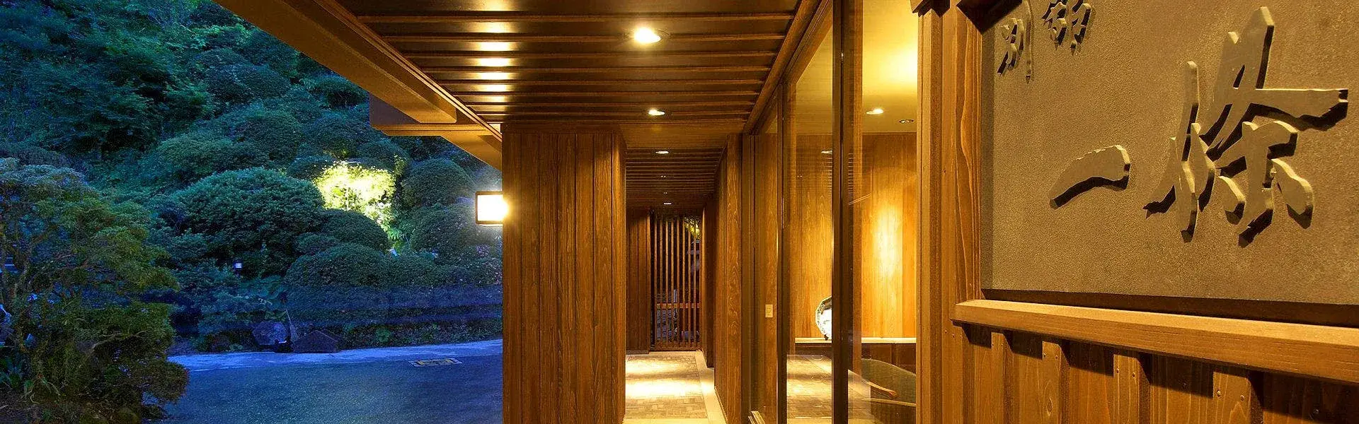 Yumushi Ichijo's illuminated entrance corridor at night, forested hillside of Shiroishi behind