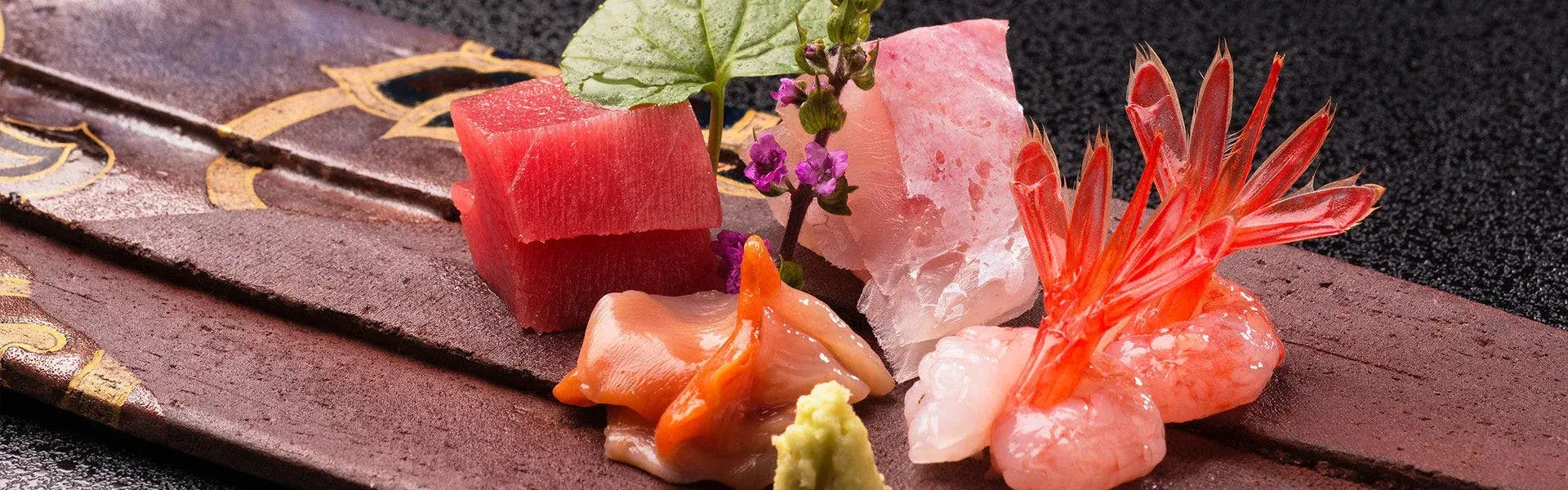 Sashimi of tuna, white fish, and botan shrimp on dark lacquerware with shiso flower