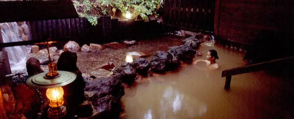 Taenoyu's lantern-lit rotenburo at night, iron-spring mineral water beside a rocky waterfall