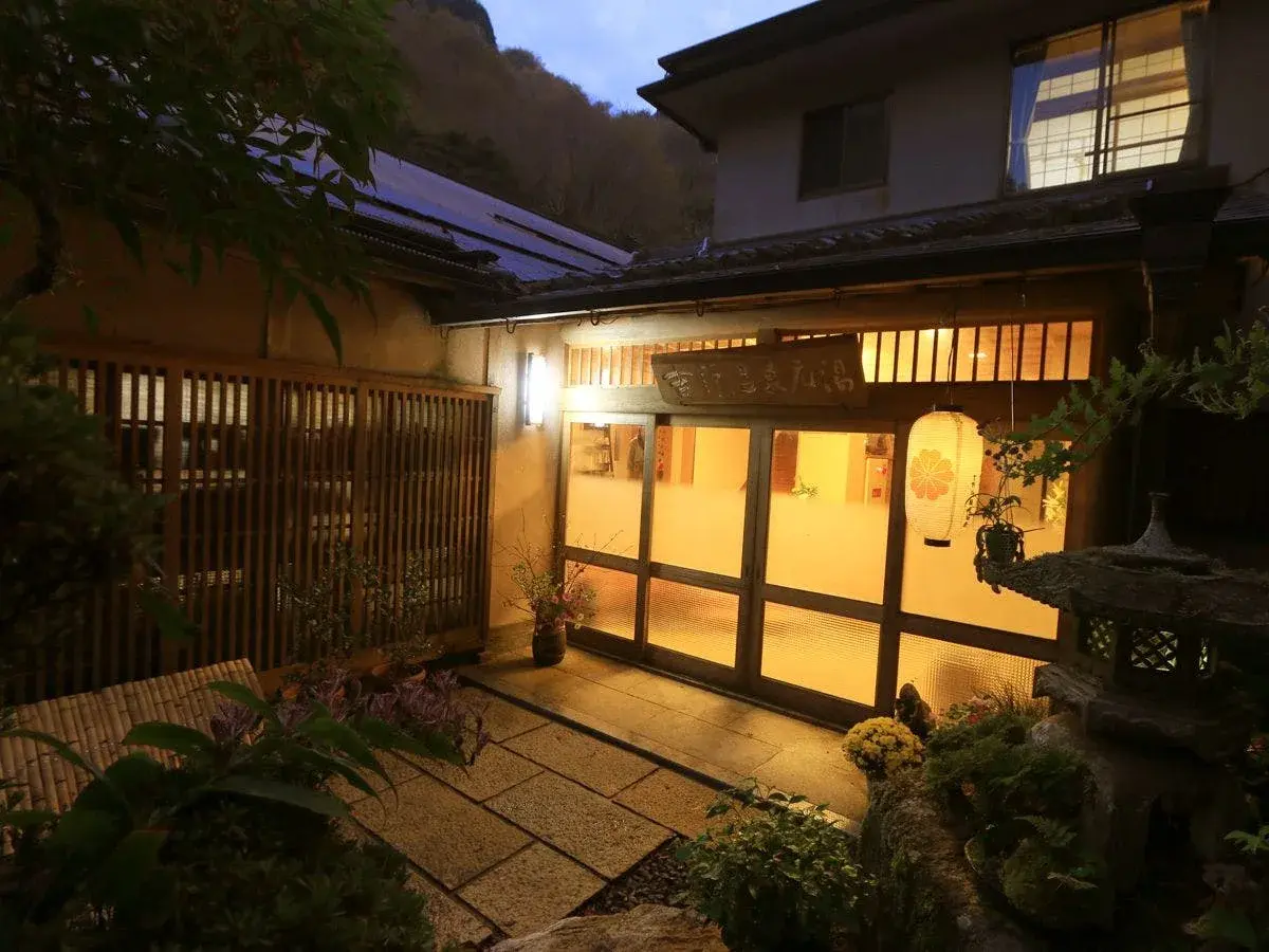 Motoyu's lantern-lit entrance at dusk, wooden lattice gate and stone garden