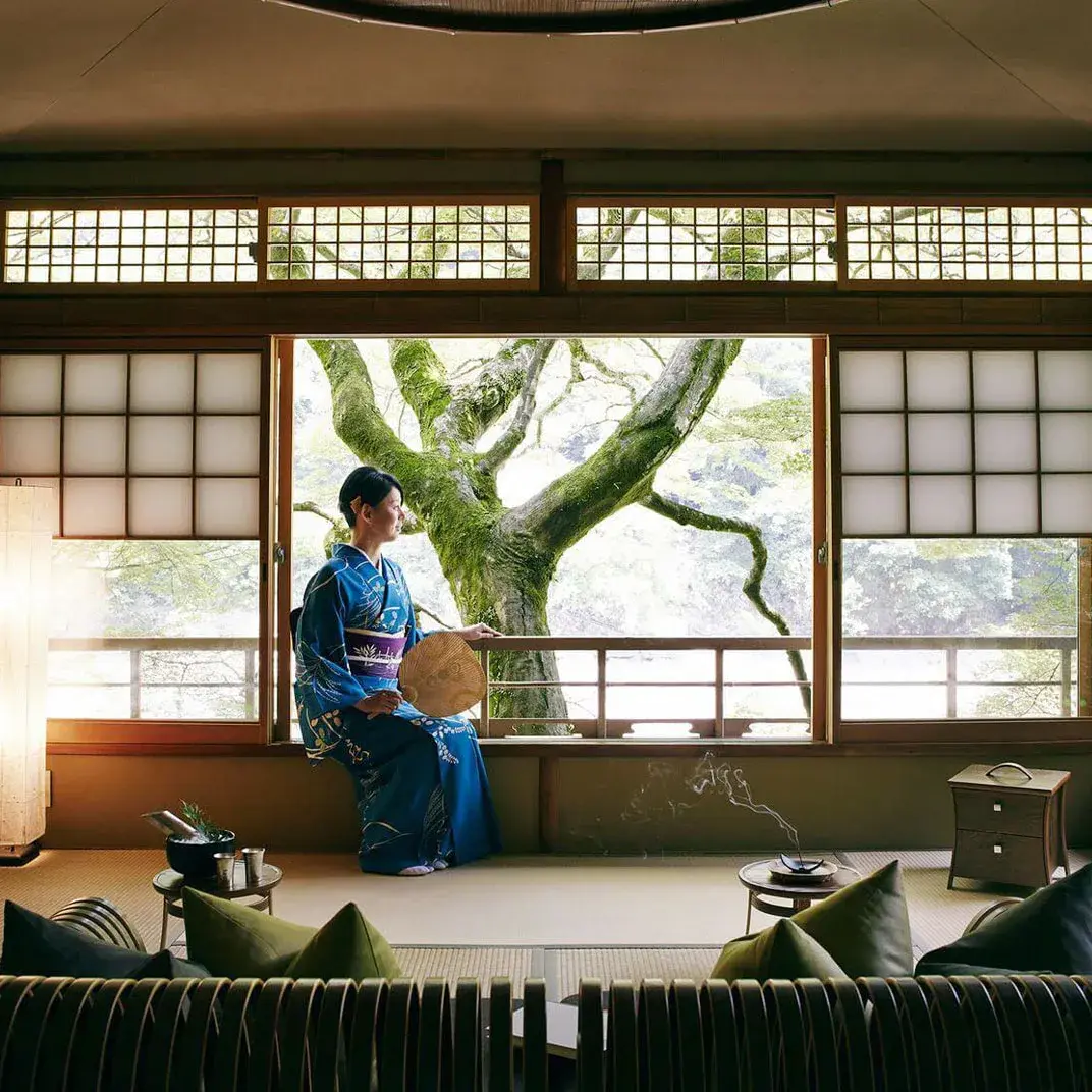 Guest in blue kimono beside shoji screens overlooking a moss-covered tree