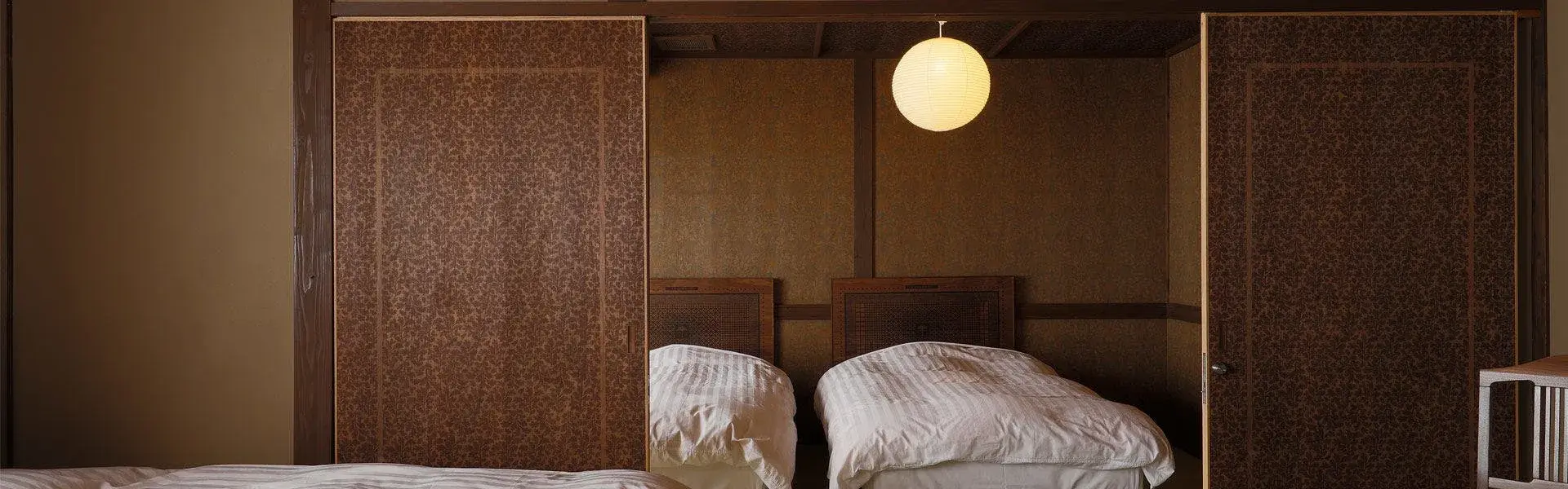 Twin room with dark textured woven panels and paper globe pendant lamp