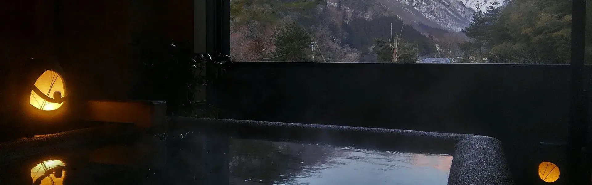 Indoor onsen with paper lantern and snow-dusted mountain view at dusk