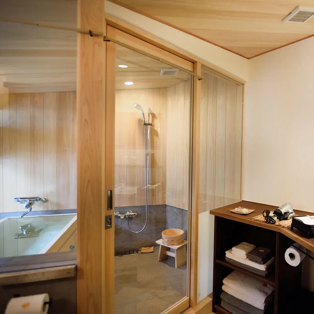 Hinoki-paneled private bath with wooden bucket and stone-tiled shower at Ryokan Kurashiki