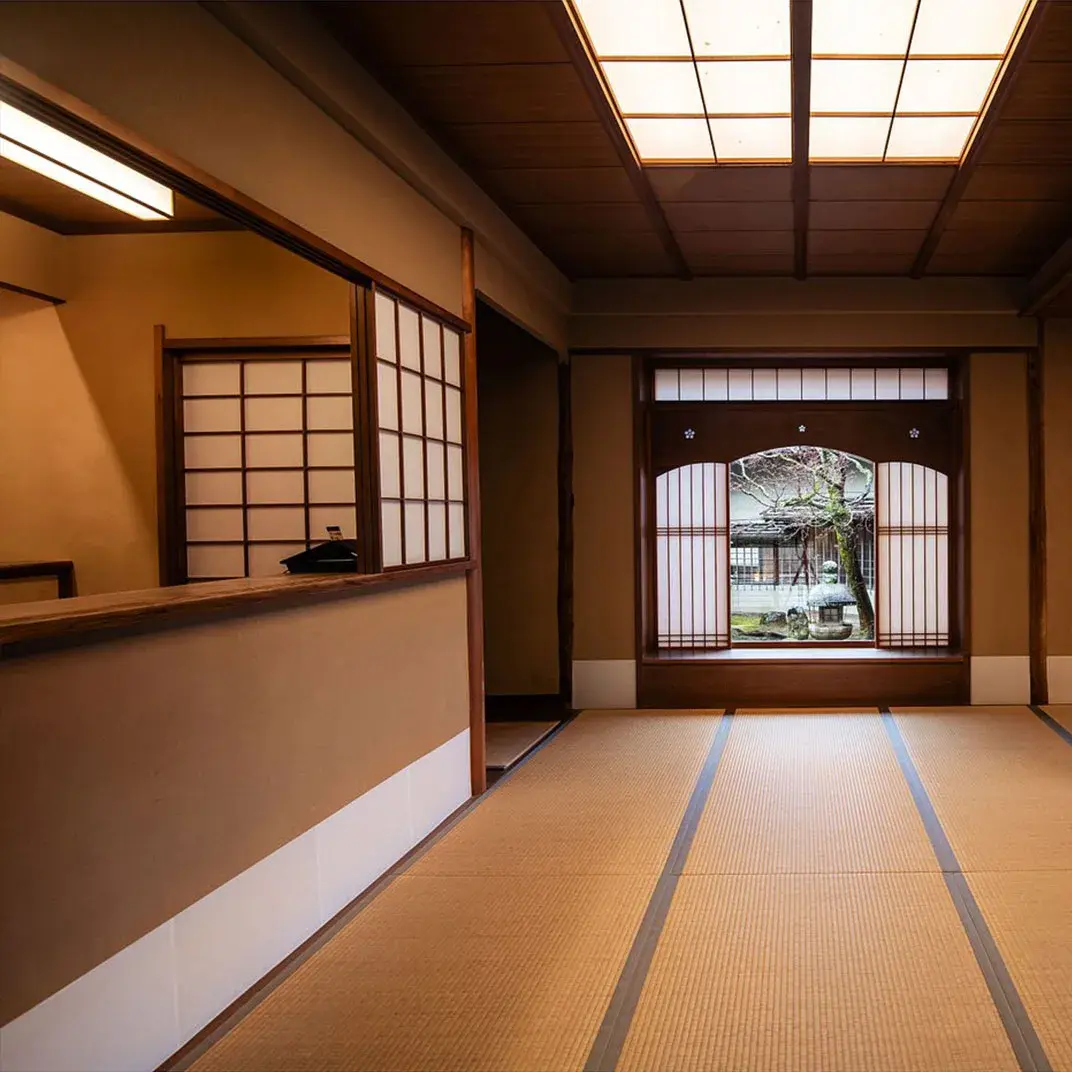 Tatami corridor at Monjusou Shourotei opening through an arched wooden gate to the courtyard