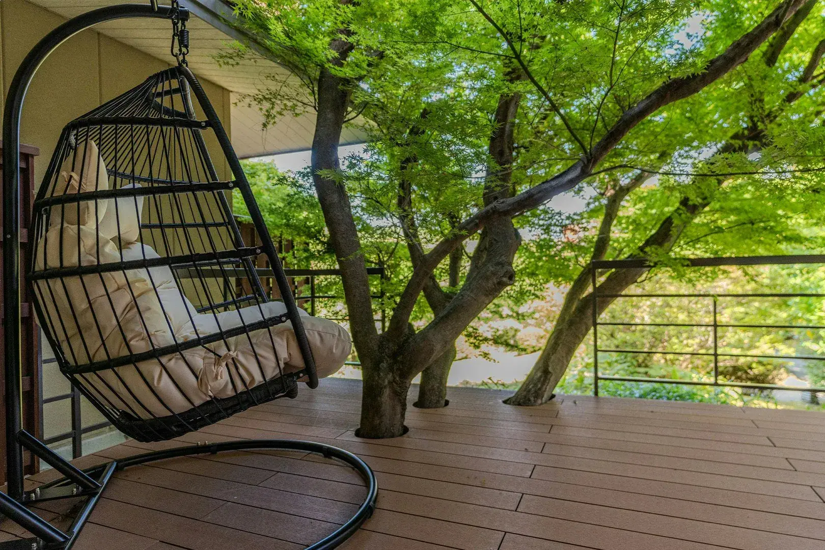 Hanging wicker chair on forest deck canopied by summer maple at Gyokusui