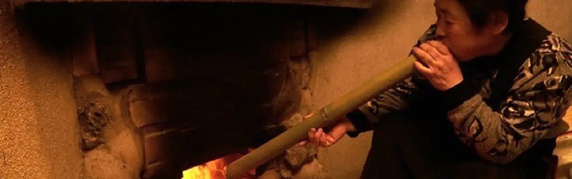 Stoking the wood-fired hearth with a bamboo blowpipe at Aso no Yamaboushi