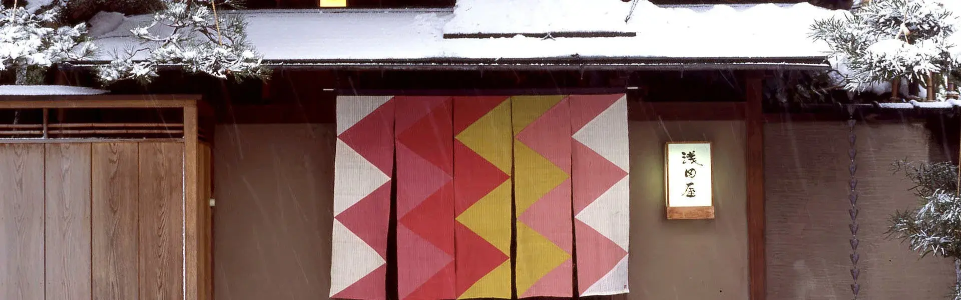 Asadaya's winter entrance in Kanazawa with geometric red and gold noren under snow