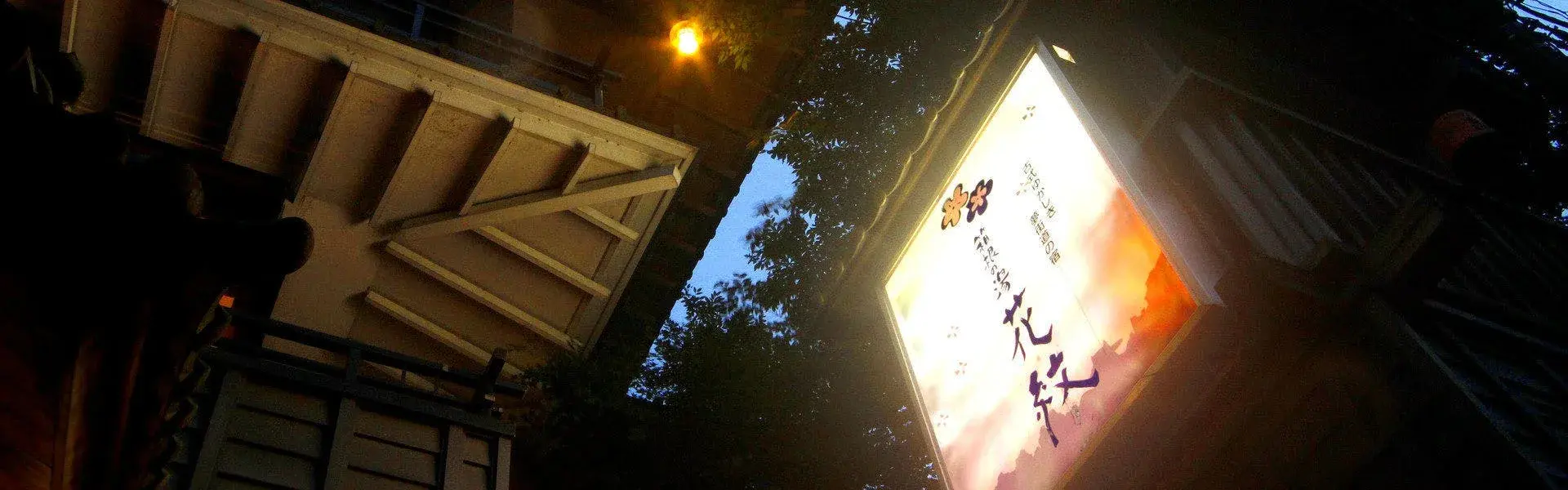 Hakone Kamon's illuminated entrance sign glowing beneath tall trees at night