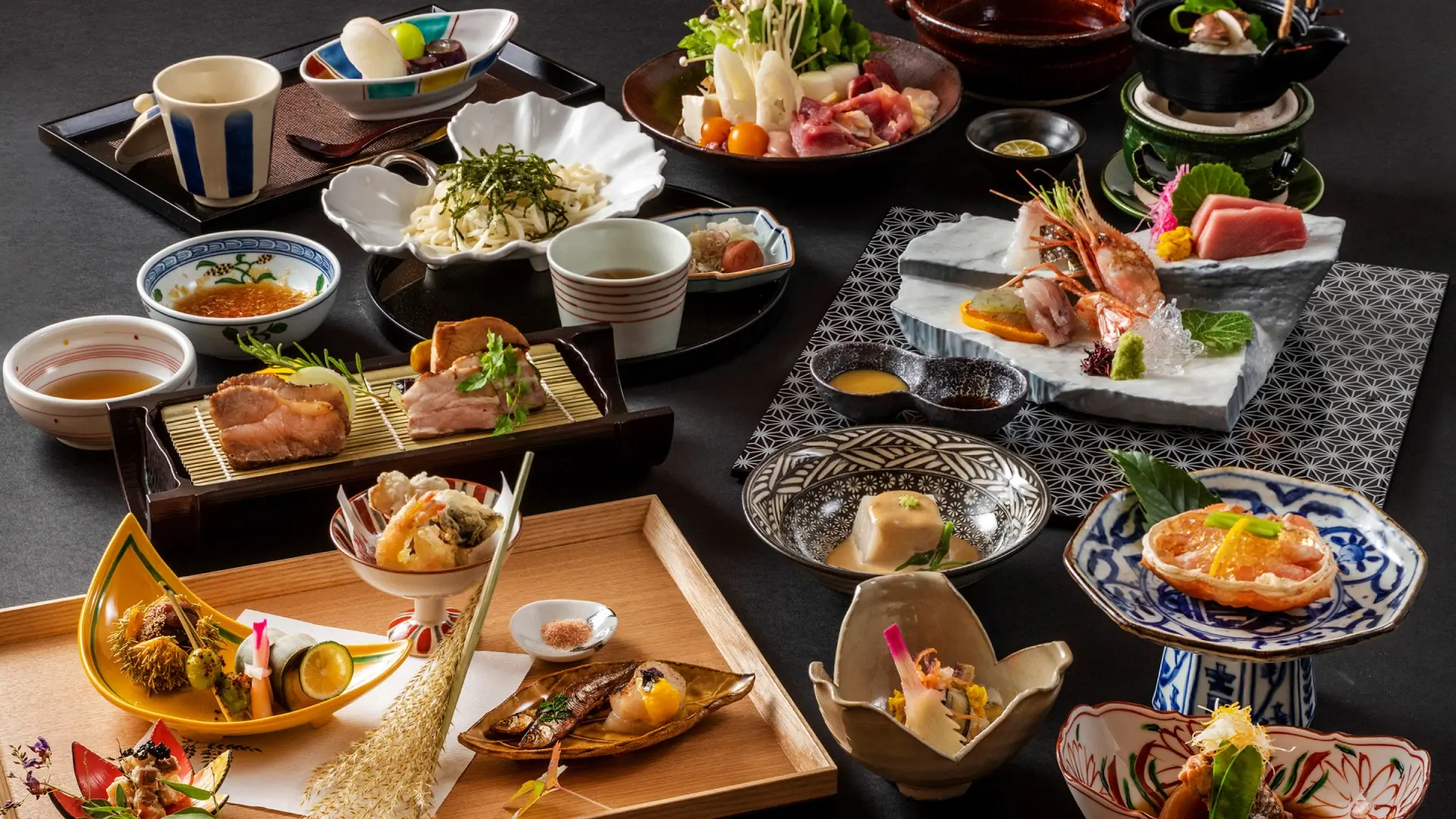 An elaborate kaiseki dinner spread with grilled fish, sashimi, simmered vegetables, and seasonal garnishes arranged across varied ceramic dishes
