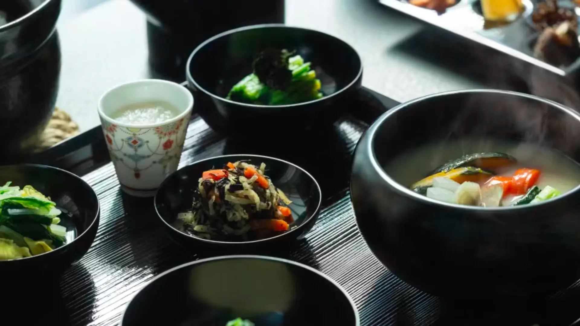 A traditional Japanese ryokan breakfast served in dark lacquer bowls with miso soup, simmered vegetables, pickles, and steamed rice
