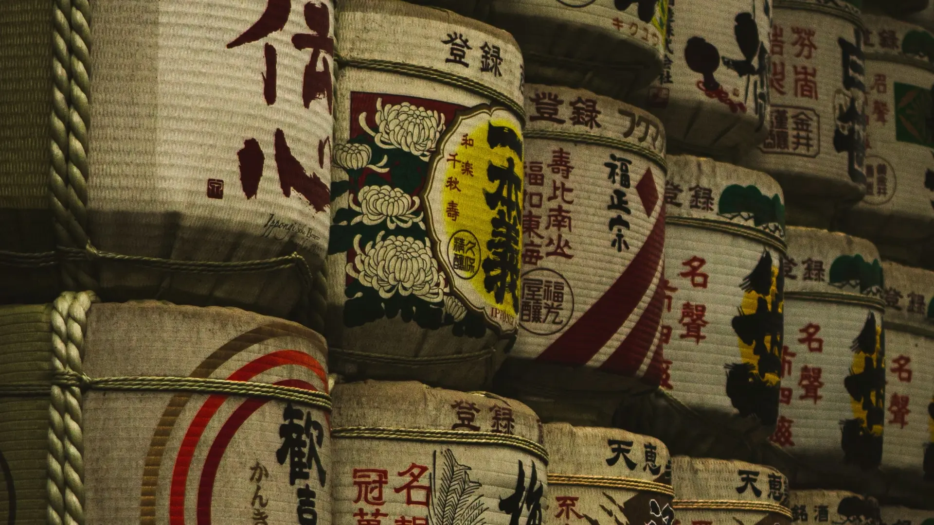 Rows of decorative sake barrels with hand-painted kanji and chrysanthemum motifs stacked at a shrine